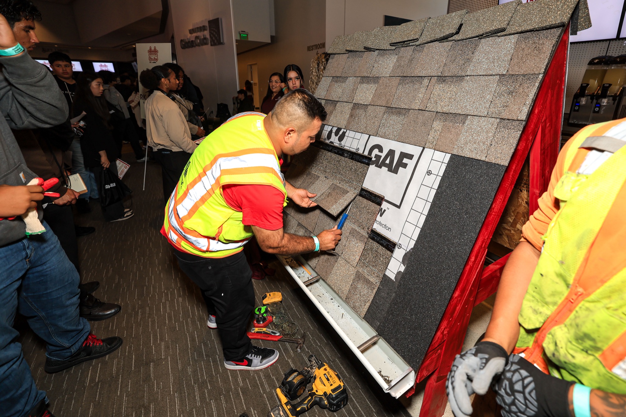 A roofer shows students how to lay shingles on a demonstration roof
